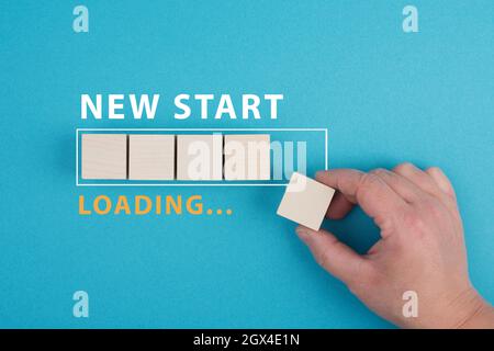 Mots nouveau départ avec une barre de chargement, la main met le dernier cube en bois sur le fond bleu Banque D'Images