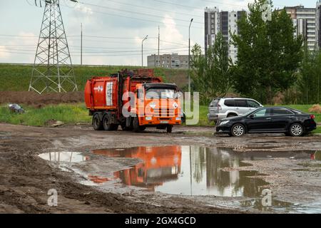 Un camion à ordures de Recycling Company se déplace autour d'une flaque près de voitures garées dans un quartier résidentiel lors d'une journée d'été nuageux. Banque D'Images