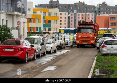 Camion à ordures et travailleurs de la compagnie de recyclage près d'un immeuble d'appartements parmi les voitures garées par une journée d'été nuageuse. Banque D'Images