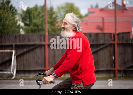 triste vieux barbu, homme à vélo portant un chandail rouge, les cheveux volant dans le vent Banque D'Images