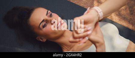 Top vue rapprochée jeune femme sportive en haut couché sur le tapis début de la période fin de l'entraînement sportif en plein air look sur la montre-bracelet. Un mode de vie sain Banque D'Images