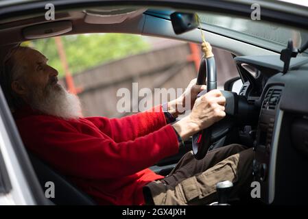 Ancien retraité senior homme avec une longue barbe conduisant une voiture grise Banque D'Images