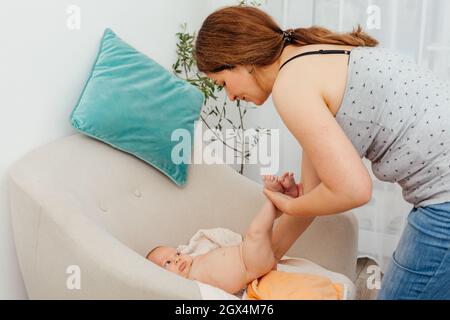 La mère change de couche réutilisable sur son bébé sur la chaise Banque D'Images