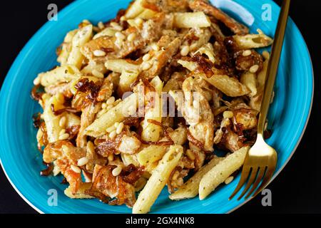 gros plan du poulet alfredo pasta penne avec oignon caramélisé arrosé de pignons de pin et de parmesan râpé sur une assiette bleue sur fond noir Banque D'Images