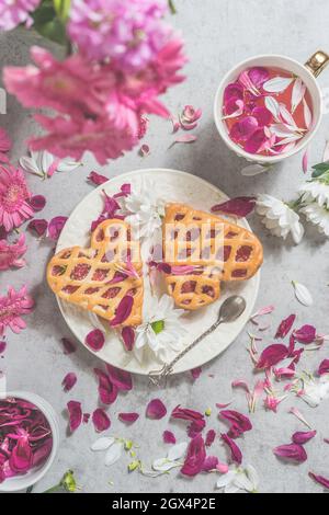 Deux gâteaux de coeur sur table légère avec une tasse de thé de fleurs roses, bouquet de pivoines et de nombreux pétales. Vue de dessus Banque D'Images