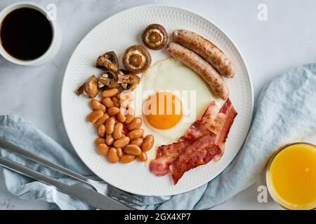 Petit déjeuner anglais classique avec œufs, saucisses, becon, haricots, champignons, café et jus d'orange Banque D'Images