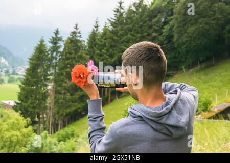 Gros plan sur l'arrière d'un jeune homme dans le parc et en photographiant la vue à l'aide de son smartphone Banque D'Images
