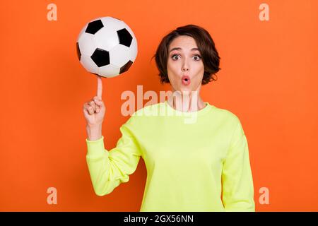 Portrait de jolie fille gaie stupéfait boule de rotation sur l'index ayant plaisir isolé sur fond orange vif Banque D'Images