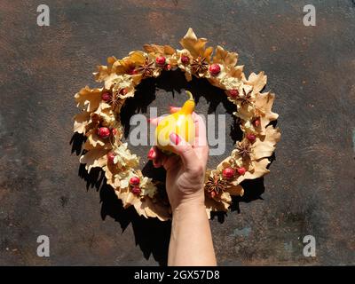 Couronne de fleurs séchées de feuilles et de baies d'automne sèches. Revêtement plat sur fond texturé brun foncé. Main avec ongles rouges manucurés tient décoratif Banque D'Images