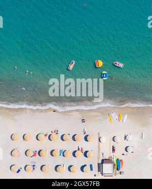 Plage de sable vue aérienne directement au-dessus, vue verticale. Chaises longues, parasols et équipement de sports nautiques, personnes nageant et prenant des bains de soleil Banque D'Images