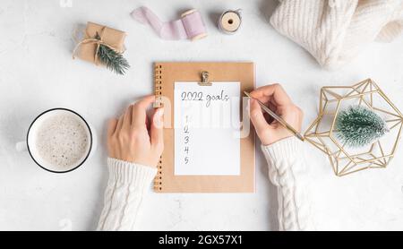 Bureau de femmes mains avec bloc-notes vierge écrire 2022 buts texte . Fond de table de travail blanc plat avec tasse de café et Noël Banque D'Images