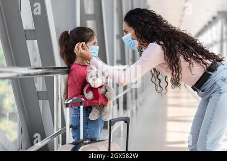 Mum affectueux ajustement du masque médical de protection sur le visage de la petite fille à l'aéroport Banque D'Images