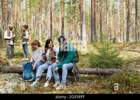 Portrait complet de divers groupes d'amis prenant la pause tout en appréciant la randonnée dans la forêt, se concentrer sur trois personnes assis sur le journal, l'espace de copie Banque D'Images