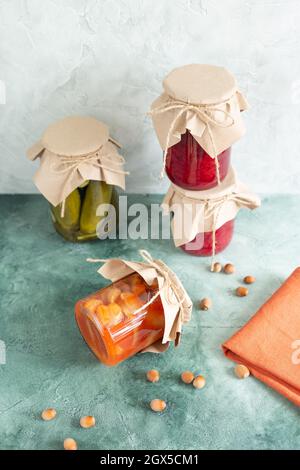 Cornichons, légumes en conserve dans des pots en verre, un pot sur le côté, des noix éparses et une serviette sur fond vert texturé vertical. Emballage écologique Banque D'Images