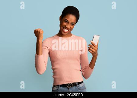 Grande chance. Femme noire pleine de joie célébrant le succès avec un smartphone entre les mains, Banque D'Images