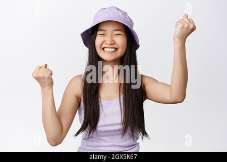 Joyeuse femme asiatique célébrant, faisant des pompes de poing et souriant satisfait, triomphant de la joie, debout sur fond blanc Banque D'Images