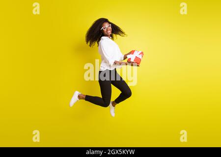 Pleine longueur corps photo femme saut en hauteur garder présent boîte sourire isolé couleur jaune vif arrière-plan Banque D'Images