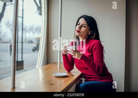 Brunette femme buvant du café tout en regardant par la fenêtre Banque D'Images
