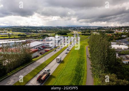 Vue de drone des camions et des voitures roulant sur la route asphaltée près des arbres verts et des bâtiments à travers la ville le jour d'été couvert. Banque D'Images