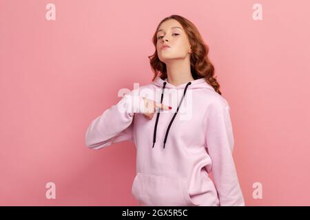 Portrait de la jeune femme égoïste brune en rose hoodie pointant le doigt sur elle-même, regardant la caméra avec arrogance et fierté. Studio d'intérieur isolé sur fond rose Banque D'Images
