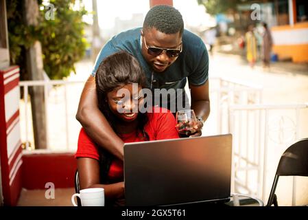 beau homme avec des lunettes de soleil debout derrière sa petite amie lui montrant une image sur l'ordinateur portable Banque D'Images