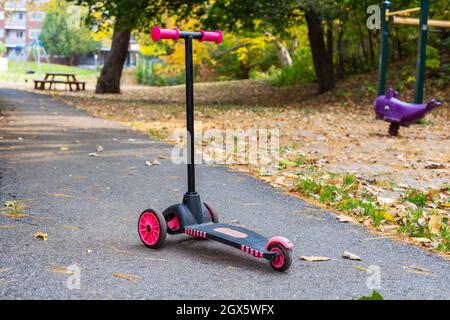 Paysage d'automne dans le parc public local avec des feuilles de couleur tombée sur le sol, aire de jeux pour enfants avec scooter sur la route. Banque D'Images