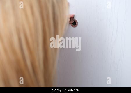 Femme regardant à travers le peephole dans la porte d'entrée de la maison fermée Banque D'Images