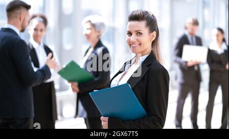 Belle jeune femme d'affaires en costume formel debout devant des collègues tenant un dossier de documents dans le bâtiment d'affaires Banque D'Images