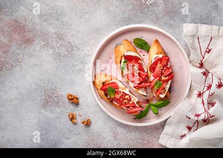 Sandwichs ouverts avec fraises, fromage doux à la menthe et aux noix dans une assiette en céramique sur fond de pierre gris clair. Nourriture estivale et saine, légumes Banque D'Images