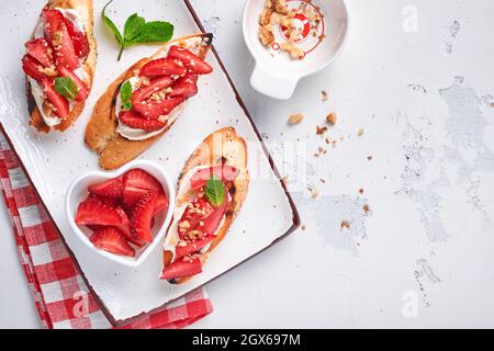 Sandwichs ouverts avec fraises, fromage doux à la menthe et aux noix dans une assiette en céramique sur fond de pierre gris clair. Nourriture estivale et saine, légumes Banque D'Images