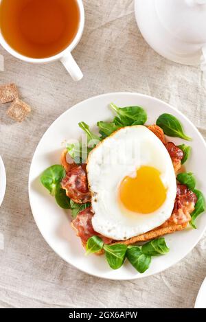 Ouvrez le sandwich avec des œufs frits, du bacon et des feuilles de légumes sur un fond clair. Vue de dessus, plan d'appartement Banque D'Images