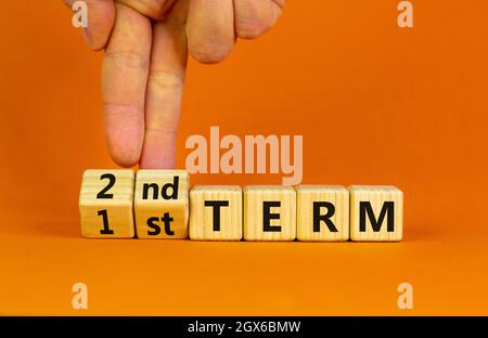 Symbole du premier ou du deuxième terme. Homme d'affaires tourne des cubes en bois et change les mots '1er terme' en '2e terme'. Belle table orange fond orange. Busi Banque D'Images