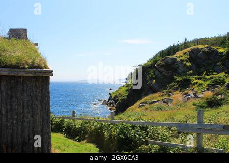 Vue sur un jardin clôturé avec vue partielle sur une maison en rondins avec un toit en gazon, sur l'océan Atlantique, New Bonaventure, NL. Banque D'Images