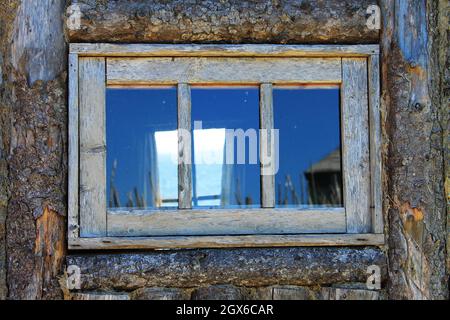 Vue à travers une vieille fenêtre encadrée en bois dans le mur d'une cabane en rondins, et à travers la fenêtre sur le mur opposé, à l'océan Atlantique. Banque D'Images