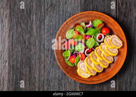 petit déjeuner au jambon et au fromage hachés petits roulés avec salade d'oignons rouges aux épinards frais sur une assiette rustique sur une table en bois, vue horizontale de Banque D'Images