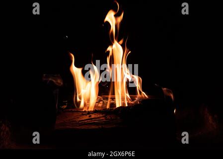 Feu dans la cheminée sur fond sombre. Bois de chauffage en flammes. Une atmosphère intime près du feu. Banque D'Images