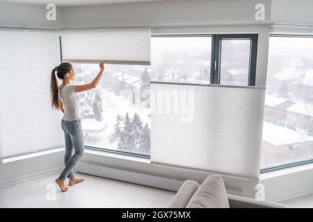 Femme ouvrant les rideaux de la maison dans l'appartement urbain. Moderne haut en bas en haut intimité nuances cellulaires sur la fenêtre de l'appartement de garder la chaleur en hiver avec Banque D'Images