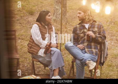 Portrait d'un jeune couple relaxant en campant dehors par une camionnette éclairée par des lumières de fées en automne, espace copie Banque D'Images