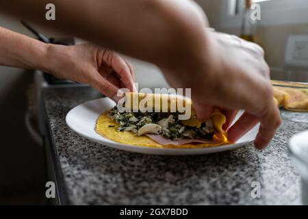 Les mains des femmes roulent de délicieux appétissants Cannelloni maison rempli d'épinards et de jambon Banque D'Images