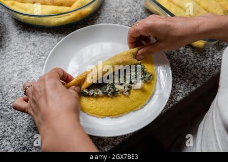 Vue de dessus des mains de femmes roulant Cannelloni maison rempli d'épinards et de jambon Banque D'Images