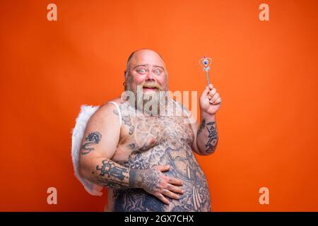 Gros homme heureux avec la barbe, tatouages et ailes agit comme une fée magique Banque D'Images