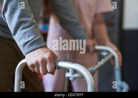 Gros plan d'un homme âgé méconnaissable utilisant un marcheur dans une maison de soins infirmiers, mobilité et expérience d'assistance, espace de copie Banque D'Images