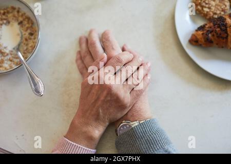 Vue de dessus gros plan d'un couple senior attentionné tenant les mains à la table du dîner, espace pour les copies Banque D'Images