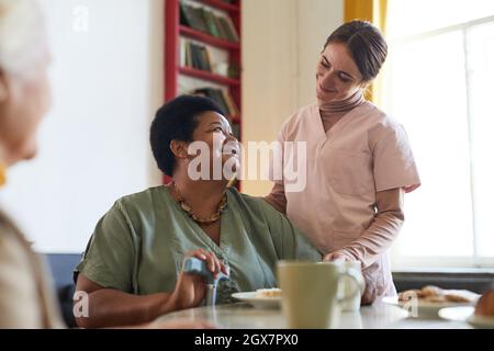 Portrait d'une jeune femme souriante assistant une patiente pendant le dîner à la maison de soins infirmiers, espace de copie Banque D'Images