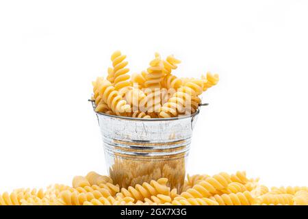 Gros plan sur des pâtes Fusilli jaune vif non cuites dans un réservoir de zinc sur fond blanc. Banque D'Images