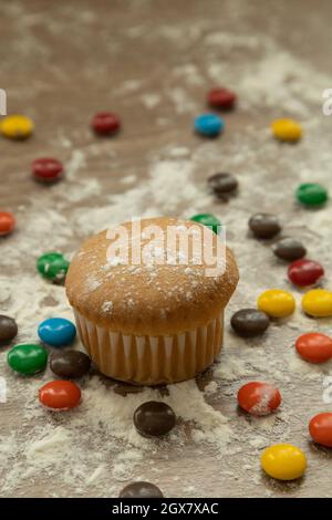 muffin sucré cuit à côté de plusieurs chocolats colorés, saupoudrés de sucre sur une table en bois, desserts délicieux, nourriture en studio Banque D'Images