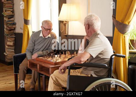 Portrait de deux hommes seniors jouant aux échecs et profitant d'activités dans une maison de repos confortable Banque D'Images