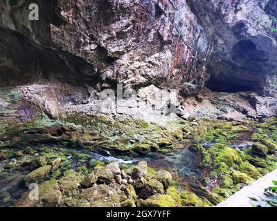 Entrée étroite d'une grotte avec de l'eau coulant sur des rochers mousseux en face Banque D'Images