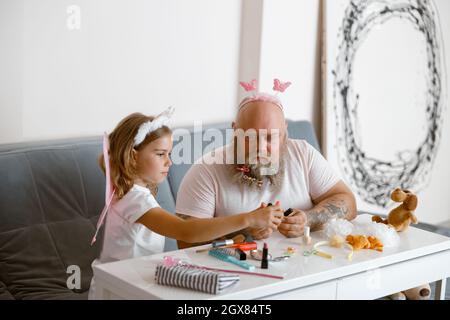 Petite fille mignonne avec papa barbu choisissez le vernis à ongles dans le salon contemporain Banque D'Images