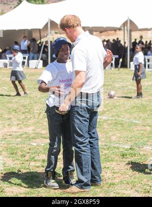 Le prince Harry salue son vieil ami Mutsu Potsane, aujourd'hui âgé de 15 ans, avec un câlin dans le parc du Centre pour enfants Mamohatho pour enfants atteints du VIH et du sida lors d'une visite de retour au Lesotho en Afrique australe le 26 novembre 2015.Au cours de la visite, le prince a parlé avec amour de la perte de sa mère, Diana, la princesse de Galles et du « trou béant » qu'il avait laissé dans sa vie. Banque D'Images